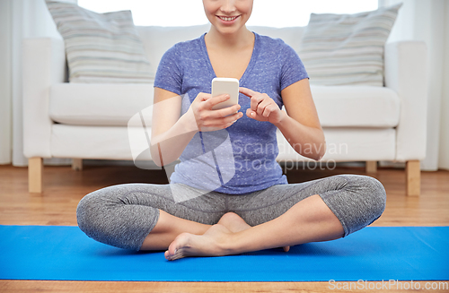 Image of woman with smartphone sitting on mat at home