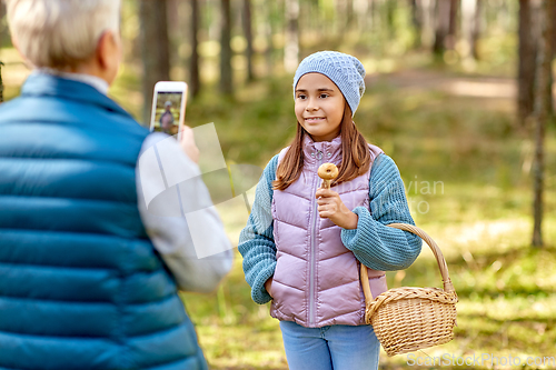 Image of grandma photographing granddaughter with mushrooms