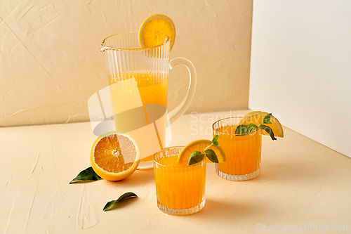 Image of glasses with orange juice and peppermint on table