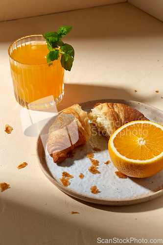 Image of glass of orange juice and croissant on plate