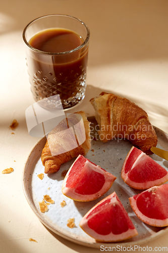 Image of glass of coffee, croissant and grapefruit on table