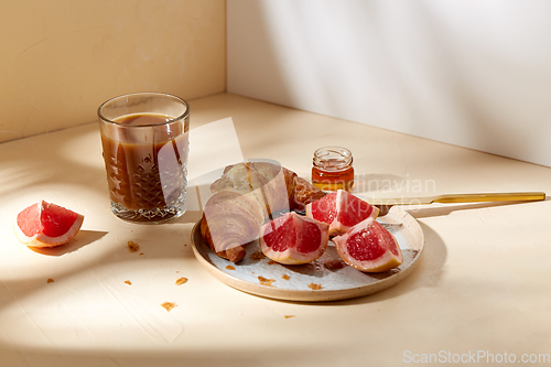 Image of glass of coffee, croissant and grapefruit on table