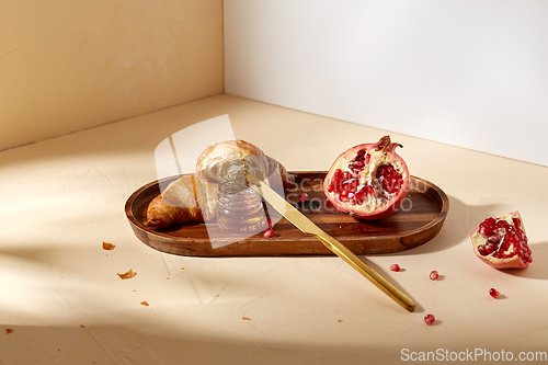 Image of croissant, pomegranate and honey on wooden tray