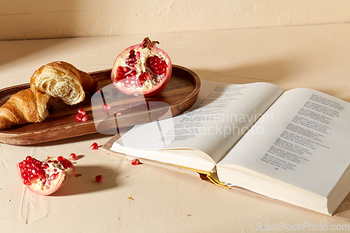 Image of book, croissant, pomegranate and honey on tray