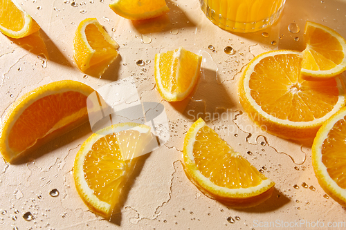 Image of glass of juice and orange slices on wet table