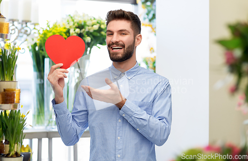 Image of smiling young man with red heart at flower shop