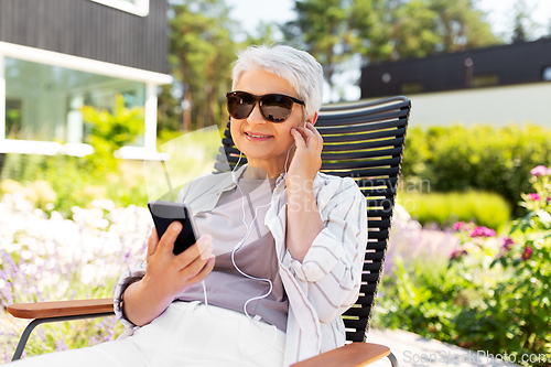 Image of old woman with earphones and smartphone at garden