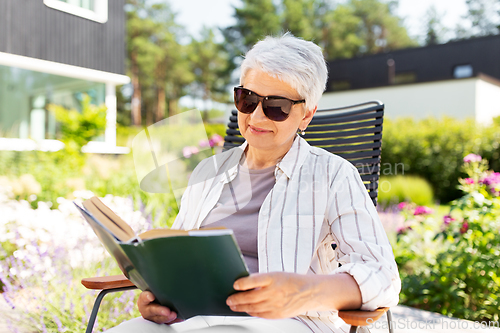 Image of happy senior woman reading book at summer garden