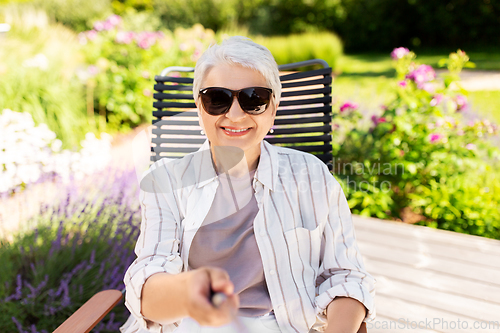 Image of happy senior woman taking selfie at summer garden