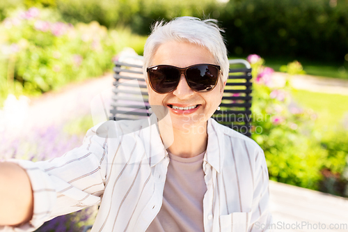 Image of happy senior woman taking selfie at summer garden