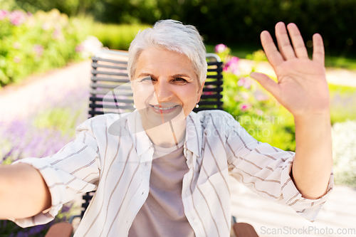 Image of happy senior woman taking selfie at summer garden