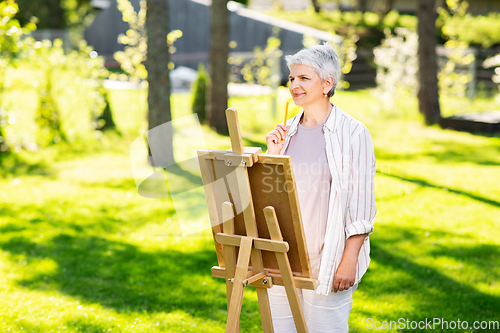 Image of senior woman with easel drawing outdoors