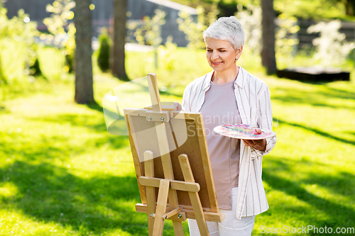 Image of senior woman with easel painting outdoors