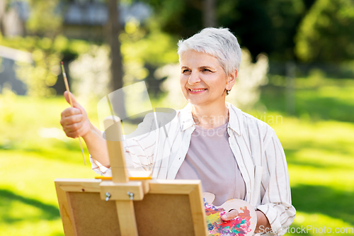 Image of senior woman with easel painting outdoors