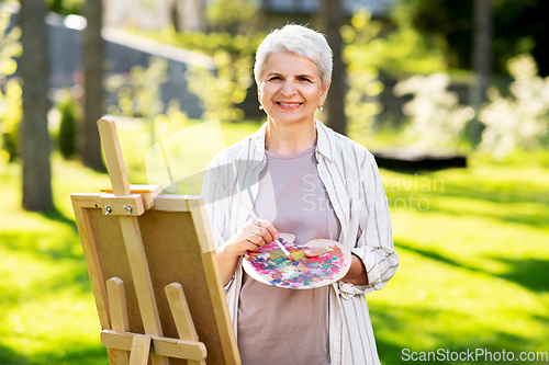 Image of senior woman with easel painting outdoors