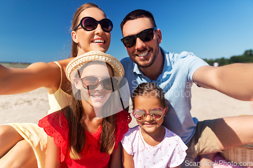 Image of happy family in sunglasses taking selfie on beach
