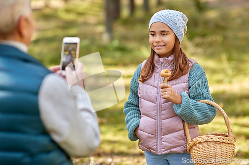 Image of grandma photographing granddaughter with mushrooms