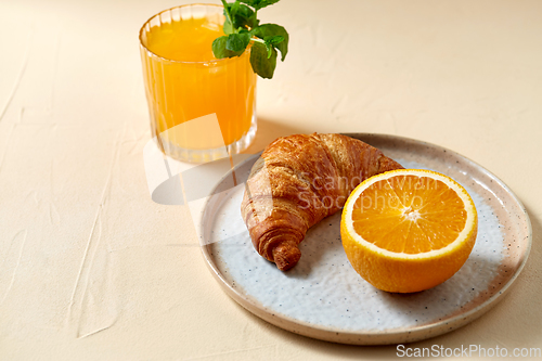 Image of glass of orange juice and croissant on plate