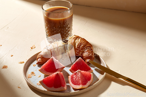 Image of glass of coffee, croissant and grapefruit on table