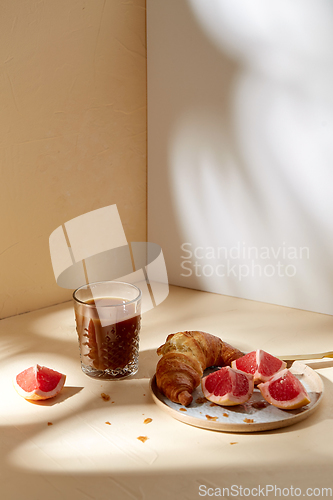 Image of glass of coffee, croissant and grapefruit on table