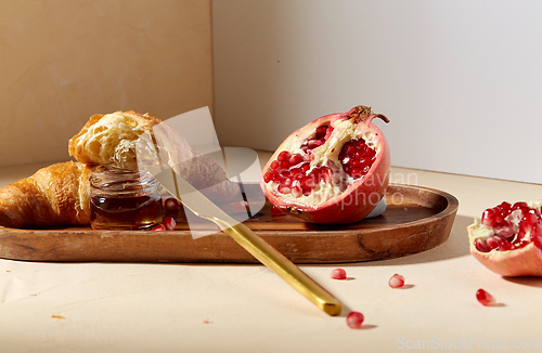 Image of croissant, pomegranate and honey on wooden tray