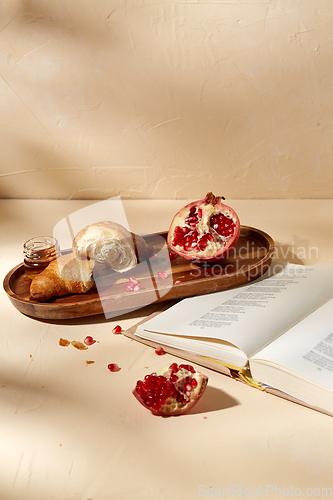 Image of book, croissant, pomegranate and honey on tray