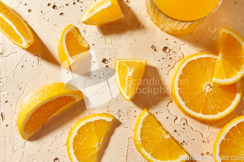 Image of glass of juice and orange slices on wet table