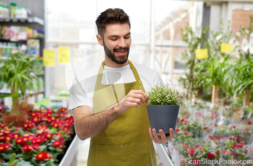 Image of smiling male gardener with flower in pot at shop