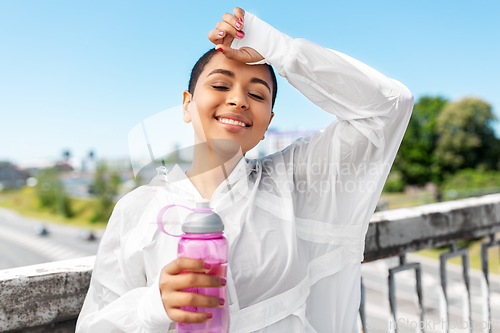 Image of african american woman drinking water from bottle