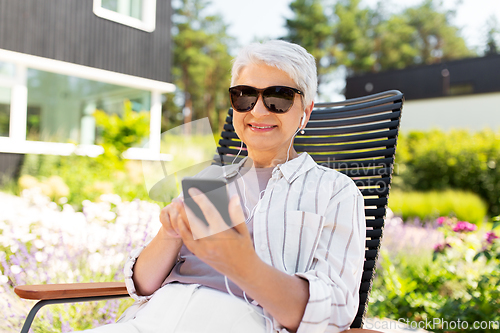 Image of old woman with earphones and smartphone at garden