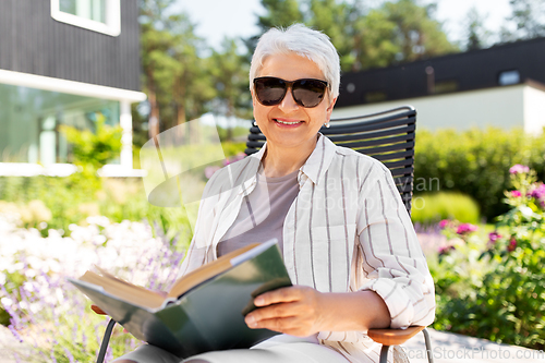 Image of happy senior woman reading book at summer garden