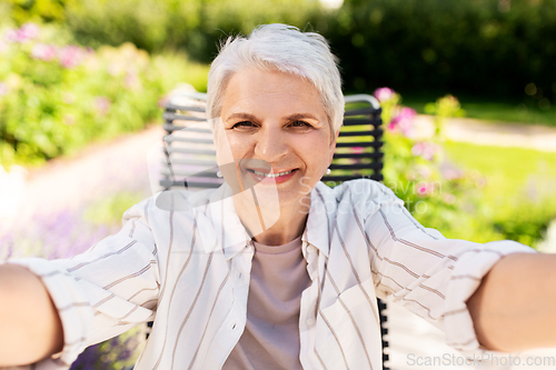 Image of happy senior woman taking selfie at summer garden