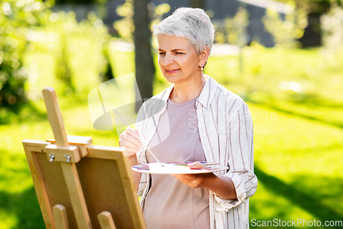 Image of senior woman with easel painting outdoors