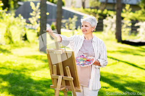 Image of senior woman with easel painting outdoors