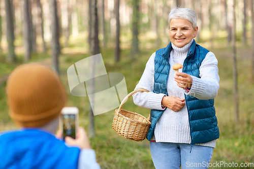 Image of grandson photographing grandmother with mushroom