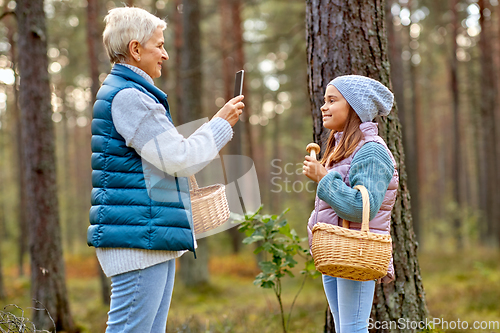 Image of grandma photographing granddaughter with mushrooms