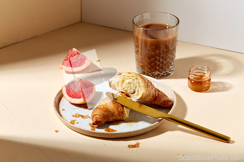 Image of glass of coffee, croissant and grapefruit on table