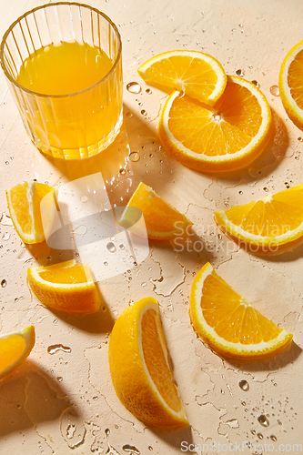 Image of glass of juice and orange slices on wet table