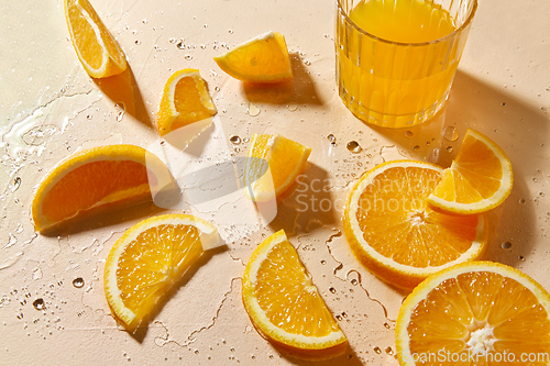 Image of glass of juice and orange slices on wet table