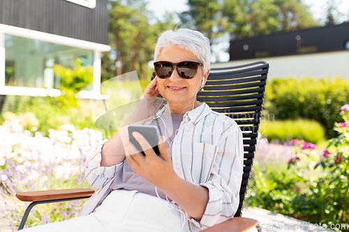 Image of old woman with earphones and smartphone at garden