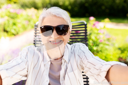 Image of happy senior woman taking selfie at summer garden