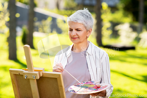 Image of senior woman with easel painting outdoors