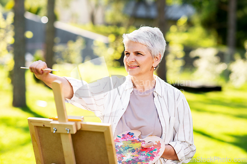 Image of senior woman with easel painting outdoors