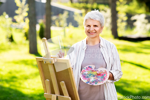 Image of senior woman with easel painting outdoors