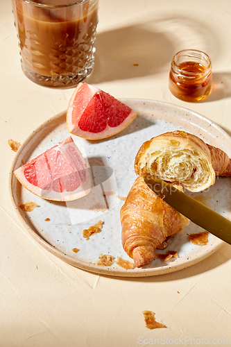 Image of glass of coffee, croissant and grapefruit on table