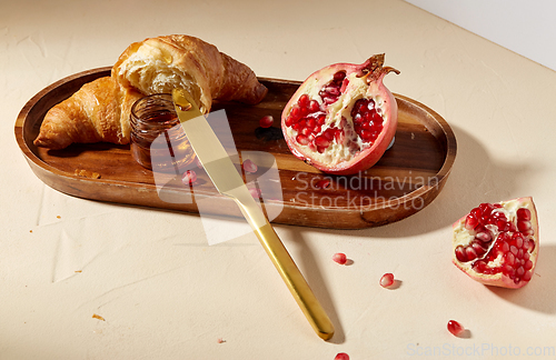 Image of croissant, pomegranate and honey on wooden tray