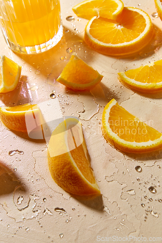 Image of glass of juice and orange slices on wet table