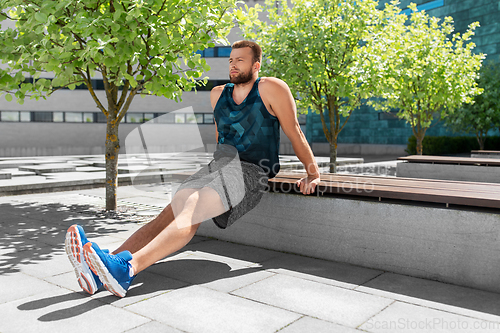 Image of young man doing triceps dip on city street