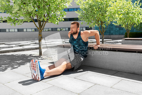 Image of young man doing triceps dip on city street