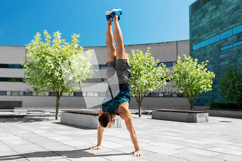 Image of young man exercising and doing handstand outdoors